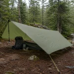 Lightweight camping tarp pitched with trekking poles over a backpacking shelter in a forest campsite